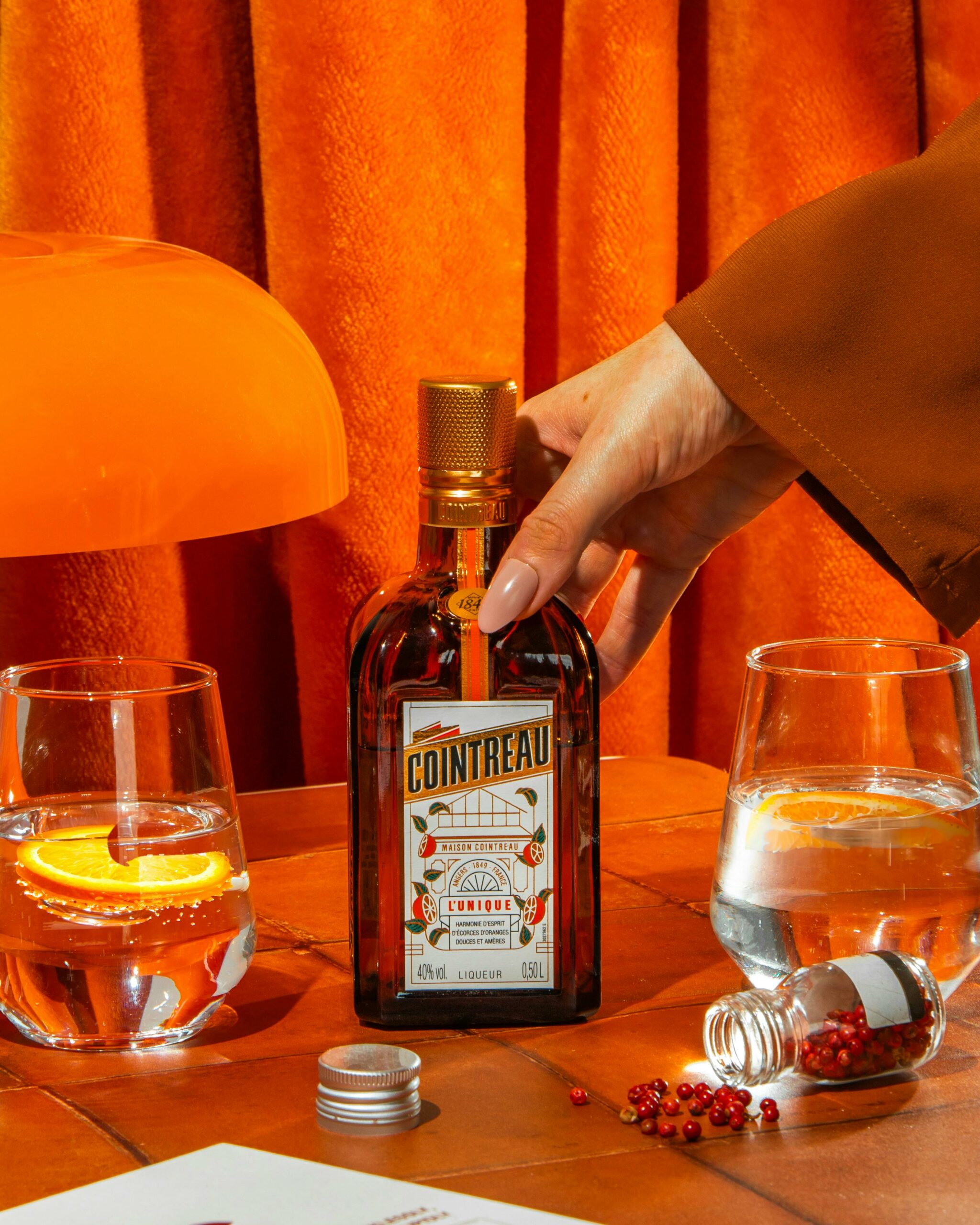 Vibrant setup featuring Cointreau bottle and citrus cocktail on an orange background.